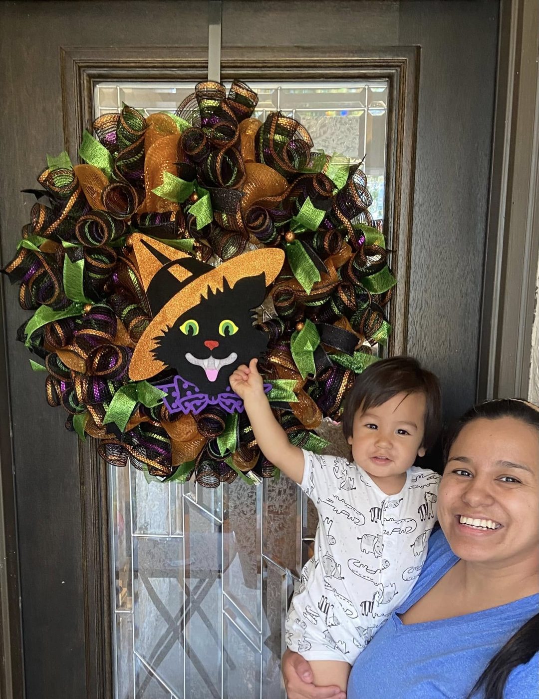 Oralia and her son holding up a black cat Halloween wreath